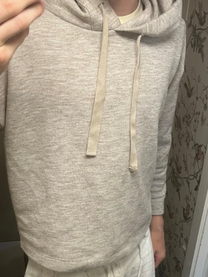 Beige hoodie med huva och snören - Säljer en stilren beige hoodie med huva och breda snören. Hoodien har en avslappnad passform och är gjord i mjukt, stickat material. Kontakta gärna om du är sugen