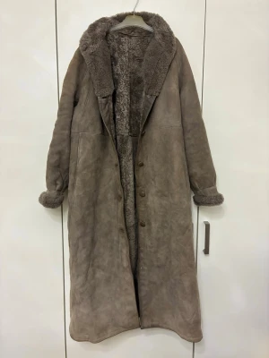 Äkta shearling Herde Pälsen kappa stl 42 – varm vinterkappa - Supervarm och tung kappa i äkta shearling (fårskinn) från Herde Pälsen i gråbrun färg. Storlek 42 och i mycket fint skick. Perfekt vinterkappa som håller dig riktigt varm och har en tidlös klassisk stil.