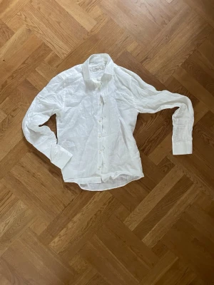 Vit linneskjorta från Dressmann  - Klassisk vit skjorta från Dressmann i 100% linne. Skjortan har lång ärm, knappar framtill och en avslappnad passform. Perfekt för en clean och fräsch look. Storlek XS.