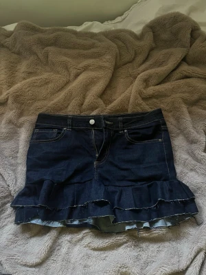 Mörkblå jeanskjol med volanger - Snygg mörkblå jeanskjol med volanger. Storlek 38/M