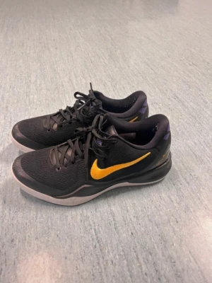  Nike basketskor kobe’s - Säljer ett par svarta basketskor från Nike med gul swoosh på sidan och lila detaljer vid hälen. Skorna har snörning, låg profil och slitstark sula. Perfekta för basket eller streetwear. Materialet är mesh och syntet för bra andningsförmåga.