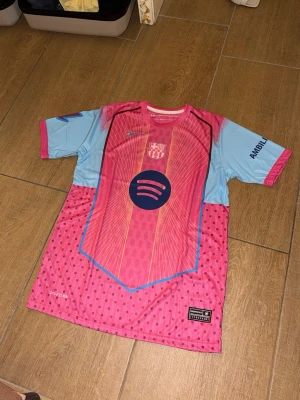 Barca matchtröja rosa/blå Lamine Yamal - Säljer en Barcelona matchtröja i rosa och ljusblått från Nike med tryck av Lamine Yamal och nummer 10. Tröjan har korta ärmar, klubbmärke, Spotify-logga och UNHCR-tryck. Storlek L 
