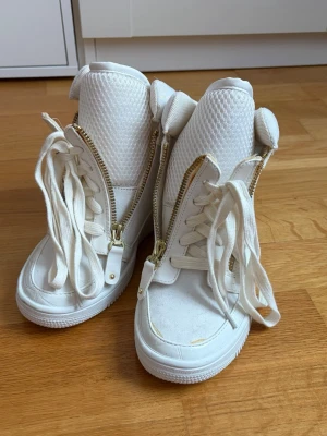 Vita high top sneakers PS for Nelly - Köpta från Sellpy men har själv aldrig använt de, de har några defekter som går att se på bilderna, tror det är lim som har spridits ut. Stilrena vita high top sneakers från PS for Nelly med grov mesh på plösen, guldfärgade dragkedjor på sidorna och klassiska vita skosnören. Skorna har en chunky look och är tillverkade i textil och syntetmaterial. Perfekta för en trendig streetstyle.