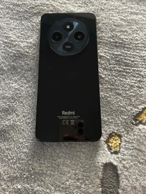 Xiaomi Redmi svart Android-mobil - Säljer en svart Xiaomi Redmi Android-telefon med HyperOS. Telefonen har en stor skärm med droppformad sensor och en rund kameramodul på baksidan med tre linser. Snygg och modern design i glas och plast, perfekt för dig som gillar stilrena mobiler.