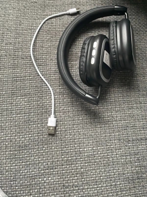 Svarta trådlösa over-ear hörlurar( Laddare ingår) - Snygga svarta over-ear hörlurar med mjuka, vadderade kåpor och justerbart huvudband. Hörlurarna har inbyggda knappar på sidan och laddas via USB-kabel som medföljer. Perfekta för musik, gaming eller videos. Modern design i plast och konstläder.