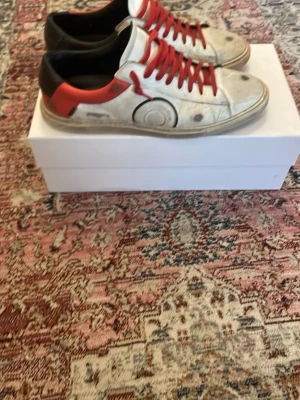 Olivier Cabell  - Tja! Säljer ett par vita sneakers från Olivier cabell med röda skosnören och detaljer i svart och rött på hälen. Klassisk siluett som passar till många olika stilar. Skorna är i bra skick utöver lite smuts som lätt går att fixa! Säljs då dem inte kommer till användning. Box o dustbag medlommer vid köp. Pris kan diskuteras vid snabb affär💯