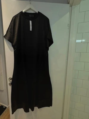 Svart långklänning från ASOS  - En stilren svart långklänning från ASOS med rund halsringning och korta ärmar. Klänningen har en rak och loose passform, vilket ger en avslappnad men ändå trendig look. 