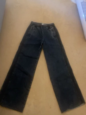 Svarta wide leg jeans med dragsko - Säljer ett par svarta jeans med breda ben och dragsko i midjan. Jeansen har klassiska fickor fram, samt råa kanter vid bensluten för en avslappnad look. Perfekta för dig som gillar en loose fit och streetstyle.helt nya Oanvända i storlek xs