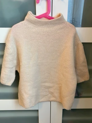 Beige stickad tröja från Gina Tricot Young - Mysig beige stickad tröja från Gina Young med hög krage och halvlånga ärmar. Tröjan har en enkel och stilren design, perfekt för lager på lager och passar till många olika outfits. Tillverkad i mjukt material som känns skönt mot huden.