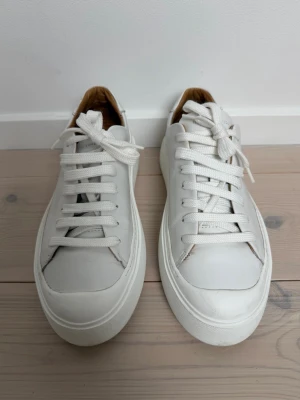Vita sneakers i läder från Tiger of Sweden - Stilrena vita sneakers från Axel Arigato i slätt läder med tjock vit sula och klassisk snörning. Insidan är fodrad i beige/brunt läder för extra komfort. Perfekta för en clean och modern look. Stor i storleken, innermått 25,7. Nypris 2500 kr.