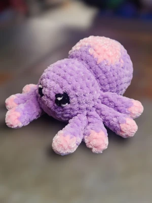Lila och rosa virkad spindel - Supermjuk och fluffig virkad spindel i lila och rosa med stora, söta ögon. Spindeln har åtta ben och är gjord av tjockt, gosigt garn som känns skönt att krama. Perfekt som dekoration eller mysig kompis i soffan.