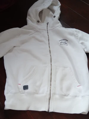 Vit hoodie från Race Marine - Säljer en vit hoodie från Race Marine med dragkedja framtill och två stora fickor. Tryck på bröstet med texten 'Scandinavian Race Marine Genuine Sportswear'. Mjuk bomullskänsla och klassisk huva med metallöljetter. Perfekt för en avslappnad stil.