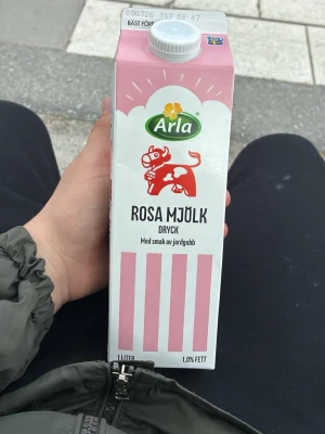 Arla Rosa Mjölk med jordgubbssmak - Säljer en 1-liters förpackning Arla Rosa Mjölk dryck med smak av jordgubb. Kartongen är vit och rosa med en söt ko-illustration och rosa ränder. Drycken innehåller 1,0% fett och har en fruktig jordgubbssmak.