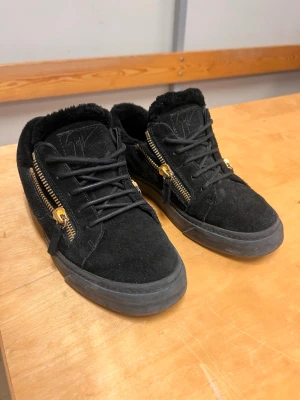 Svarta Giuseppe Zanotti sneakers - Säljer ett par svarta sneakers från Giuseppe Zanotti i mocka med guldfärgade dragkedjor på sidorna. Skorna har svarta snören, tjock sula och mjukt foder. Perfekta för dig som gillar en lyxig och edgy stil.