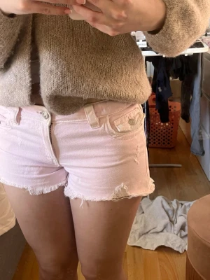 Ljusrosa jeansshorts med fransar - Säljer ett par ljusrosa jeansshorts med råa franskantade benslut och klassiska fickor fram och bak. Shortsen har knapp- och dragkedjestängning samt bälteshällor. Perfekta för varma dagar! Slutsålda på Gina därav priset!