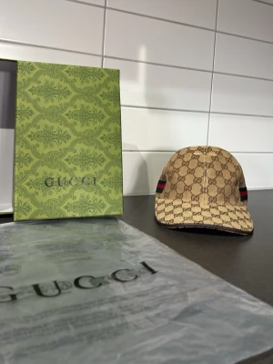 Beige keps från gg  - Snygg beige keps från Gmed klassiskt gg-monogram över hela kepsen och en grön-röd rand på sidan. Kepsen har böjd skärm och justerbar passform. Kommer med originalförpackning och tagg.jag är seriös jag lovar jag gillar inte den här färgen på Dena kepsen så köp i så fall om ni är intresserade jag gillar bara svarta😎🙏📦 postar inom cirka 45 min eller 24 timmar 📦 om ni it vill ha den då säljer jag den till min kompis jag måste bli av med den kepsen inom en månad