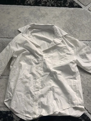 Vit klassisk skjorta med krage - Stilren vit skjorta med klassisk krage och knäppning framtill. Skjortan har lång ärm och en bröstficka. Perfekt till både jeans och kostymbyxor. 