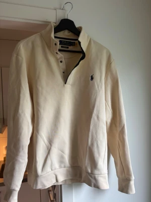 Beige tröja från Polo Ralph Lauren - Klassisk beige långärmad tröja från Polo Ralph Lauren med hög krage och knappslå. Storlek M