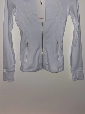 Lululemon  - Snygg vit träningsjacka från Lululemon i modellen Define Jacket. Tillverkad i stretchigt och mjukt Luon-material med dragkedja framtill, två fickor med dragkedja, tumhål och figurnära passform. Perfekt för träning eller som ett sportigt lager.