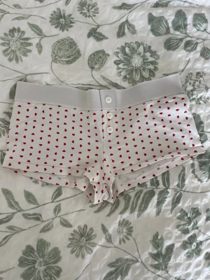 Vita pyjamas shorts med hjärtan - Vita pyjamas shorts med röda hjärtan. Mjukt och stretchigt material. Från gina tricot i storlek 146/152 passar XXS/XS. En liten fläck på framsidan men syns knappt och annars i mycket bra skick.