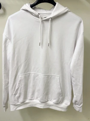Vit hoodie  - Klassisk vit hoodie med stor magficka och justerbar dragsko i huvan. Hoodien har ribbade muddar vid ärmslut och nederkant. Perfekt för en clean och avslappnad stil. Tillverkad i mjukt material för extra komfort.