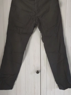 Mörkgrå din byxor med raka ben - Säljer ett par mörkgrå fin byxor med raka ben och enkel design. Byxorna har en avslappnad passform och är tillverkade i ett svalt linnematerial som passar perfekt till sommaren. Inga synliga detaljer eller fickor på framsidan.