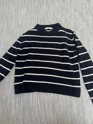 Svartvit randig stickad tröja H&M - Snygg svart stickad tröja från H&M med vita horisontella ränder. Tröjan har rund halsringning, långa ärmar och ribbade muddar vid ärmslut och nederkant. Perfekt för dig som gillar klassisk och enkel stil.