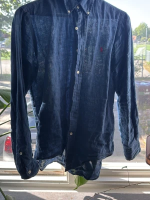 Marinblå linneskjorta från Polo Ralph Lauren - Snygg marinblå skjorta i linne från Polo Ralph Lauren. Skjortan är i bra skicka, säljer då den inte kommer till användning. Perfekt inför sommaren. Bara att höra av sig vid funderingar.