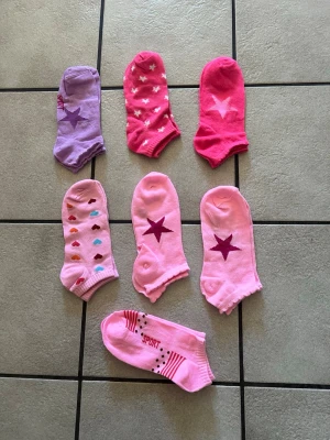 Färgglada korta strumpor med stjärnor storlek 36-38 - Sju par låga strumpor i olika nyanser av rosa och lila, dekorerade med stjärnor, hjärtan och prickar. Några har texten 'SPORT' och randiga detaljer. Perfekta för dig som gillar färg och mönster i vardagen.