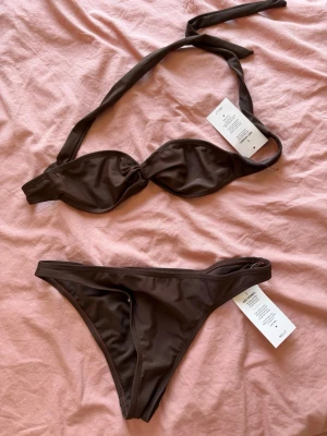 Brun bikini med knyt i sidan från Nelly - Snygg brun bikini med enkel design och knyt i sidan på underdelen. Perfekt för strandhäng eller pooldagar. Materialet känns mjukt och följsamt mot huden. Aldrig använd!