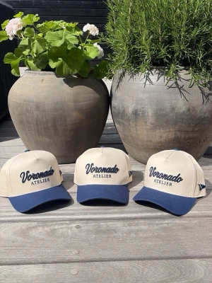 Voronado Rivera cap - Snygg keps från Voronado Atelier i beige med mörkblå skärm och broderad logga framtill. Klassisk sexpaneldesign med justerbar rem baktill. Perfekt accessoar för en avslappnad och trendig look.
