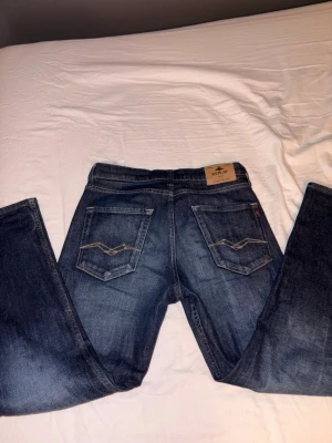 Blå jeans från Replay, modell THAD 12a - Säljer ett par snygga blå jeans från Replay i modell THAD. Klassisk femficksdesign med kontrastsömmar och Replay-lapp bak i midjan. Jeansen har rak passform och är tillverkade i slitstarkt denimtyg. Perfekta för dig som gillar stilrena och tidlösa jeans. Helt nya. Nice för sommaren 