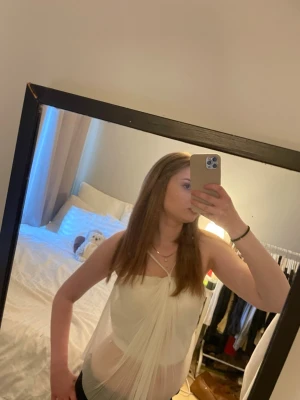 Vit axelbandslös bandeau topp - Säljer en vit axelbandslös bandeau topp med draperad effekt framtill. Tunn och luftig, perfekt för varma dagar. Stilen är trendig och passar dig som gillar att sticka ut. Materialet känns som syntet och toppen är ärmlös.