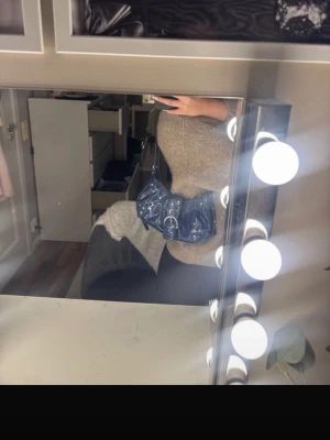 Blå axelväska i lack med spänne - Snygg blå axelväska i glansigt lackmaterial med silverfärgat spänne framtill och dekorativa nitar. Väskan har en kort axelrem och cool, trendig form som sticker ut. Perfekt för dig som vill ha en statementväska till din outfit. använt max två gånger 