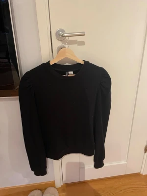 Svart långärmad tröja med puffärm - En svart långärmad tröja med puffärm och rund halsringning. Toppen har en enkel och stilren design som passar till många olika looks. Tillverkad i mjukt material för en bekväm känsla. Är storlek M men passar som en S.