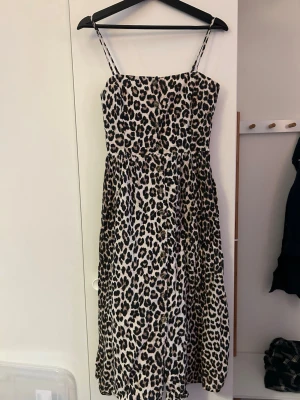 Leopardmönstrad långklänning - Säljer en snygg långklänning med leopardmönster och tunna axelband. Klänningen har knappar framtill och en lätt utställd passform. Perfekt för dig som vill sticka ut med ett djuriskt print. Materialet känns mjukt och svalt, troligen bomull eller polyester.
