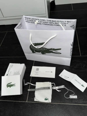 Silverfärgat armband från Lacoste - Helt ny! Allt på bilden tillkommer, storleken kan justeras och den är 21cm. Skickas så fort du köper