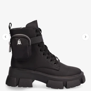 Chunky svarta boots från Steve Madden - Svarta boots med chunky sula från Steve Madden. Skorna har snörning, dragkedja på sidan och en avtagbar liten ficka med silverdetaljer. Tillverkade i syntetmaterial med rund tå och cool urban vibe. Nypris 1700