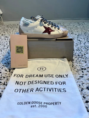 Golden goose skor storlek 37 - Jätte fina vita sneakers ifrån Golden Goose med röd glittrig stjärna och skosnören med leopard mönster. Skorna är i storlek 37, och är i mycket bra skick då de endast är använda ett fåtal gånger. Skobox, dustbag, och ”Golden goose passport” med QR kod till Golden Goose hemsida medföljer. Kontakta mig för följande frågor eller prisförslag!😊