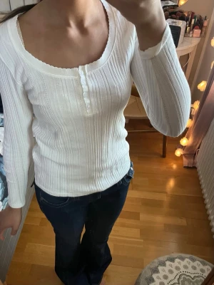 Vit ribbad långärmad topp - Säljer en vit ribbad långärmad topp med rundad halsringning och dekorativa knappar framtill. Nytt skick aldrig använd 