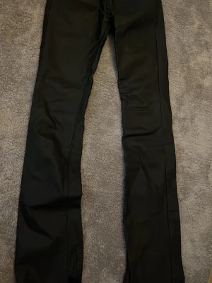 Svarta coated jeans från Estee Brown - Säljer ett par svarta coated jeans från Estee Brown. De har en slim fit-modell med raka ben och klassisk femficksdesign. Materialet har en lätt glansig finish som ger en cool look. Perfekta för dig som vill ha ett par stilrena och trendiga jeans.