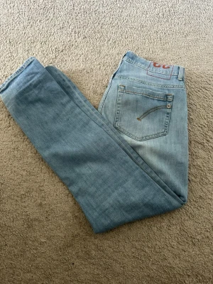 Ljusblå raka jeans från Dondup - Säljer ett par ljusblå jeans från Dondup, tillverkade i Italien. Jeansen har klassisk femficksdesign, raka ben och diskreta sömmar. Materialet är mjukt denim som ger en avslappnad look. Perfekta för dig som gillar stilrena och tidlösa jeans.