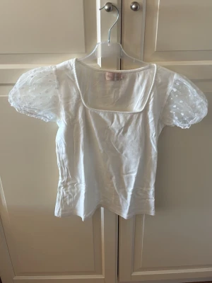 Vit topp med puffärmar och prickig tyll - Söt vit topp med transparenta puffärmar i mesh och vita prickar. Toppen har fyrkantig urringning och korta ärmar med volangkant. Storlek S. Från Chica London. I fint skick. 