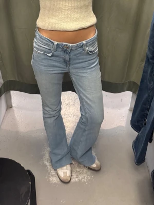 Ljusblå bootcut jeans med låg midja - Säljer ett par ljusblå bootcut jeans med låg midja och klassiska fem fickor. Jeansen har en snygg utsvängd passform och är perfekta för en avslappnad och trendig look. Materialet är mjukt denim i bomull. Från zara storlek 38, jag är 171cm