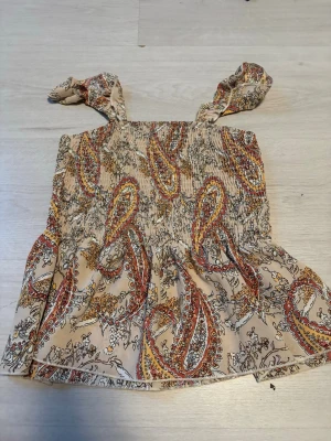 Topp shein  - Supersöt beige linnetopp från Shein med paisleymönster i rött, gult och svart. Toppen har smockad överdel och knytbara axelband för en extra gullig touch. Perfekt för varma dagar och enkel att styla med jeans eller kjol.tveka inte att höra av er vid frågor eller funderingar😇💕