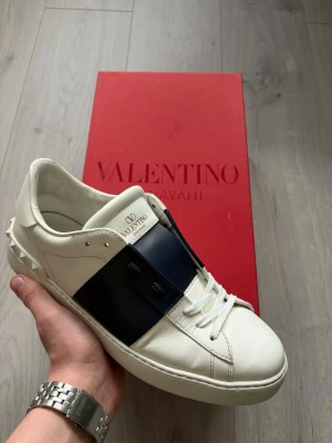 Open Sneaker - Vita Valentino Open sneakers med mörkblå detalj. Skorna är i extremt fint skick och har fått helt nya original snören. Vid köp tillkommer även skolåda och kuvert med Valentino kort. Storlek 42 kan även passa 42,5/43 då denna modell sitter något större, fråga om innermått vid intresse.