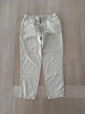 Beiga linnebyxor med dragsko - Snygga och avslappnade linnebyxor i beige med elastisk midja och dragsko. Byxorna har raka ben, sidofickor fram och bakfickor. Perfekta för en chill och stilren look under varma dagar. Tillverkade i luftigt linne för extra komfort.