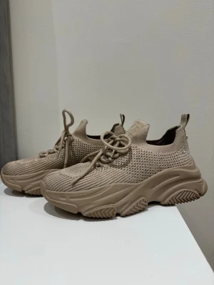 Steve madden sneakers - Säljer ett par beige chunky sneakers med stickad ovandel och grov sula. Skorna har snörning framtill och en praktisk hälflik med guldfärgad detalj. Perfekta för dig som gillar streetwear och vill ha en modern look.