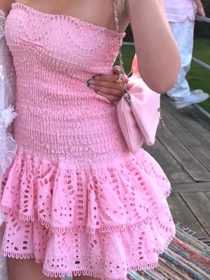 Rosa volangklänning  - Supersöt rosa kortklänning från design by amor  med smockad överdel och volangkjol i broderad bomull. Ärmlös och axelbandslös modell med romantiska detaljer och luftig känsla, perfekt för sommarens alla tillfällen. Använd 1 gång, skriv om ni har några frågor, priset kan diskuteras ❤️