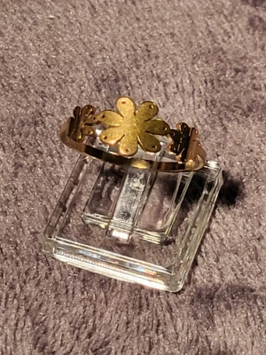 Guldfärgad ring med blomdetalj - Unik guldfärgad ring med en stor blomformad detalj i mitten och mindre blommor längs bandet. Ringen har en blank finish och är tillverkad i metall. Perfekt för dig som vill ha en söt och iögonfallande accessoar.